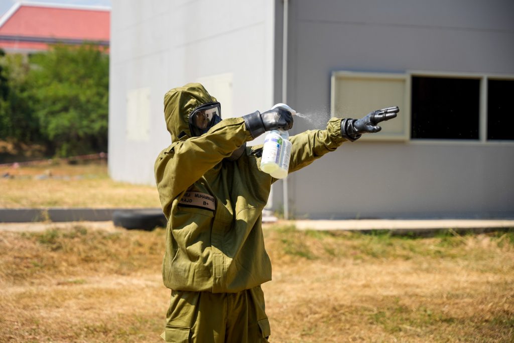 Soldier in CBRN suit using decontamination spray as part of emergency preparedness and stockpiling strategy